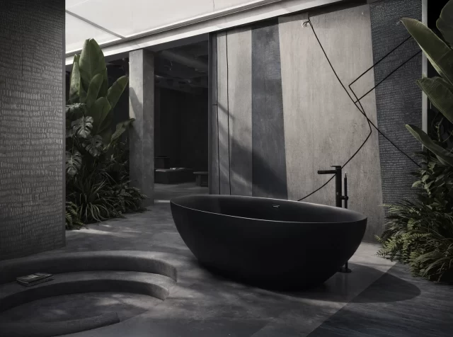 Vasca da bagno freestanding ovale a forma di mandorla in metacrilato nero opaco a doppio strato, posizionata al centro di un ambiente zen rivestito con carta da parati decorartiva, rubinetteria a pavimento cromata.